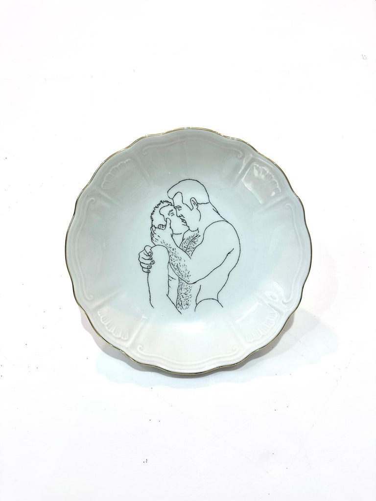 Omri Danino Porcelain Plate engraved with a drawing of older hairy man and younger man kissing, in black engraving on white plate with golden rim